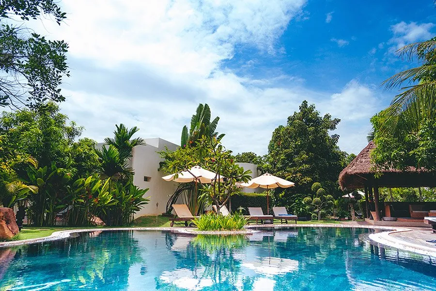 Swimming pool set in tropical gardens with thatched shade and loungers